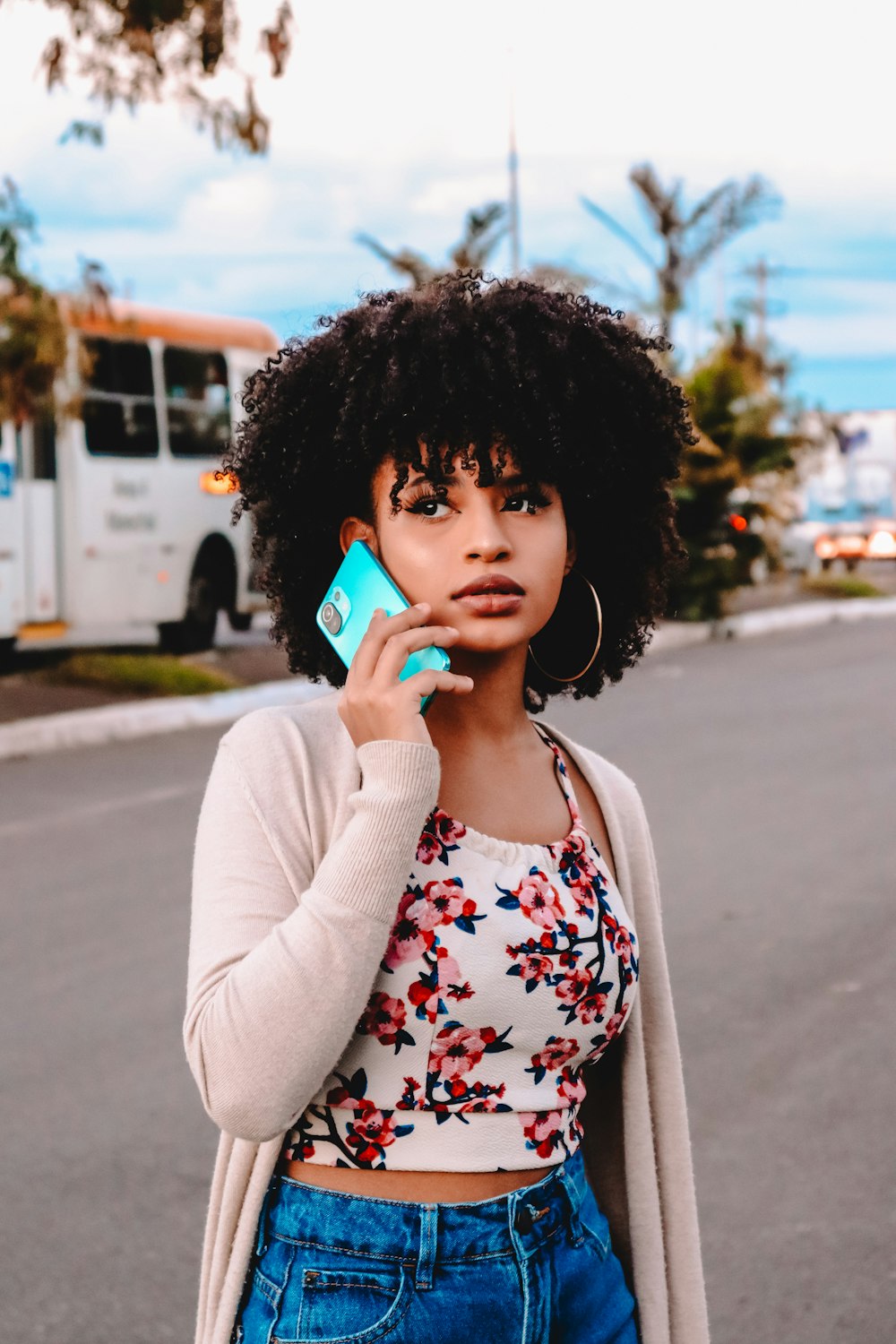 woman in white cardigan holding blue smartphone