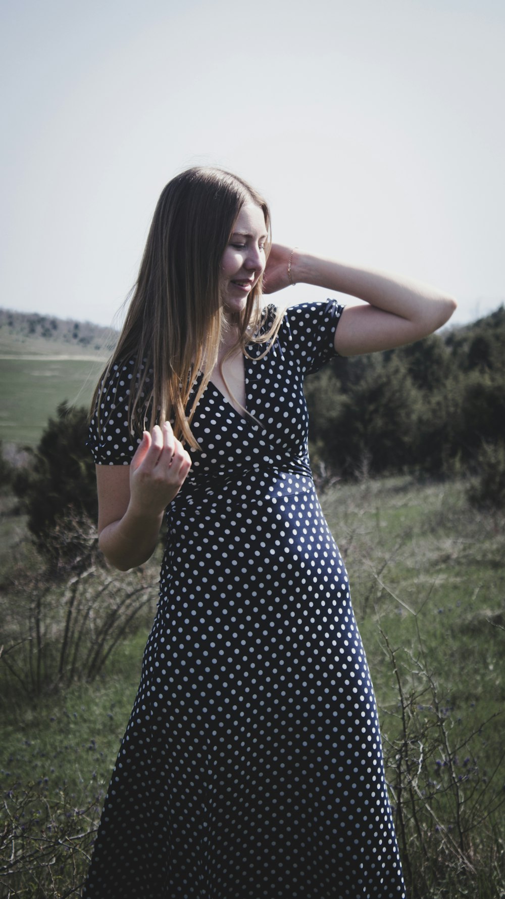 woman in black and white polka dot dress standing on green grass field during daytime