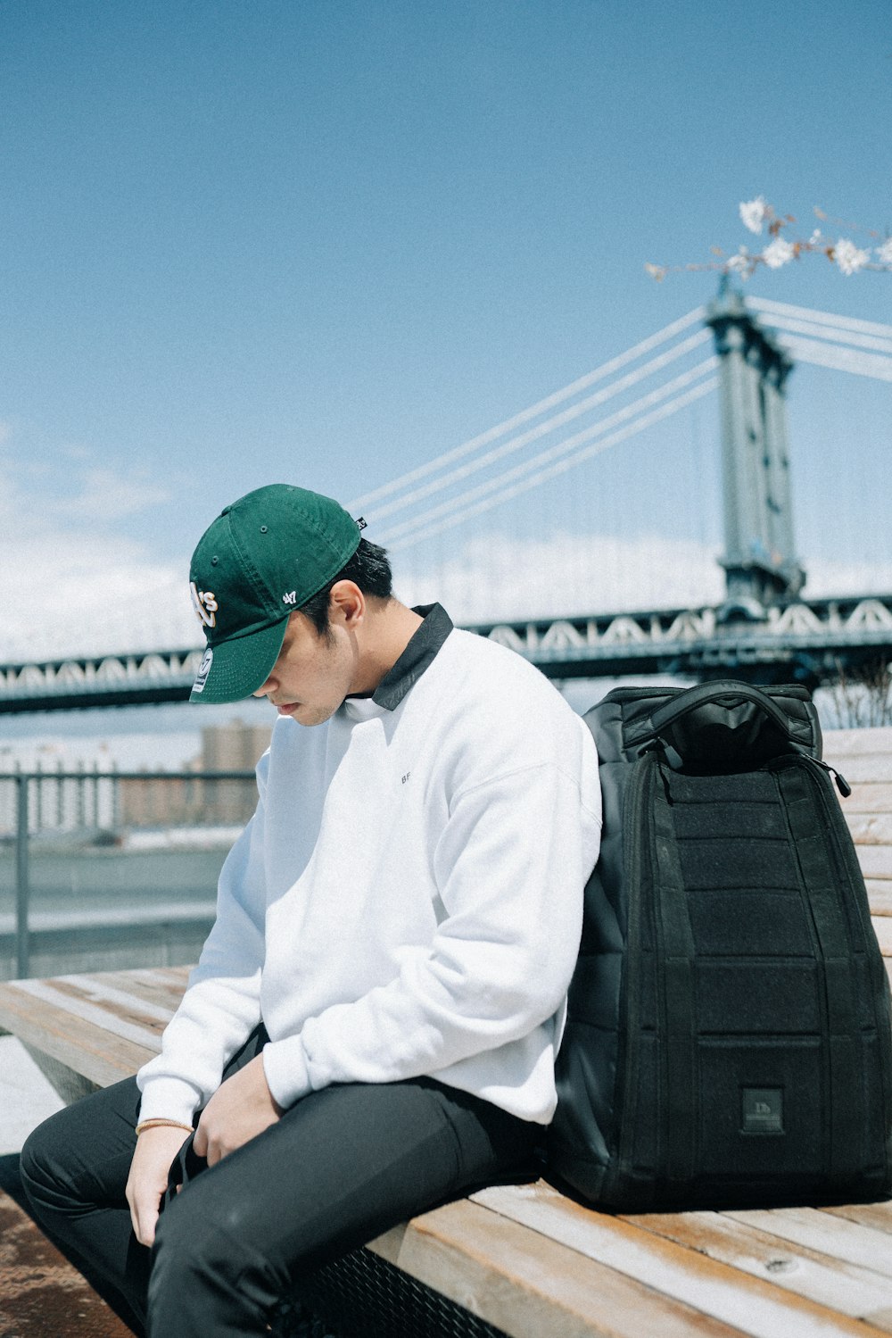 man in white dress shirt and green cap sitting on bench during daytime