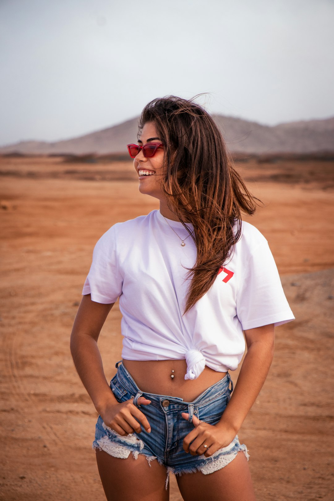 woman in white crew neck t-shirt and blue denim daisy dukes standing on brown sand