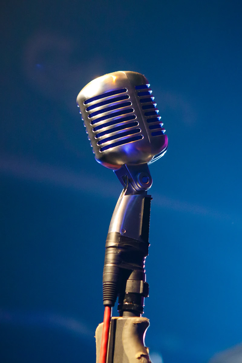 A silver vintage microphone on a stand against a solid blue background