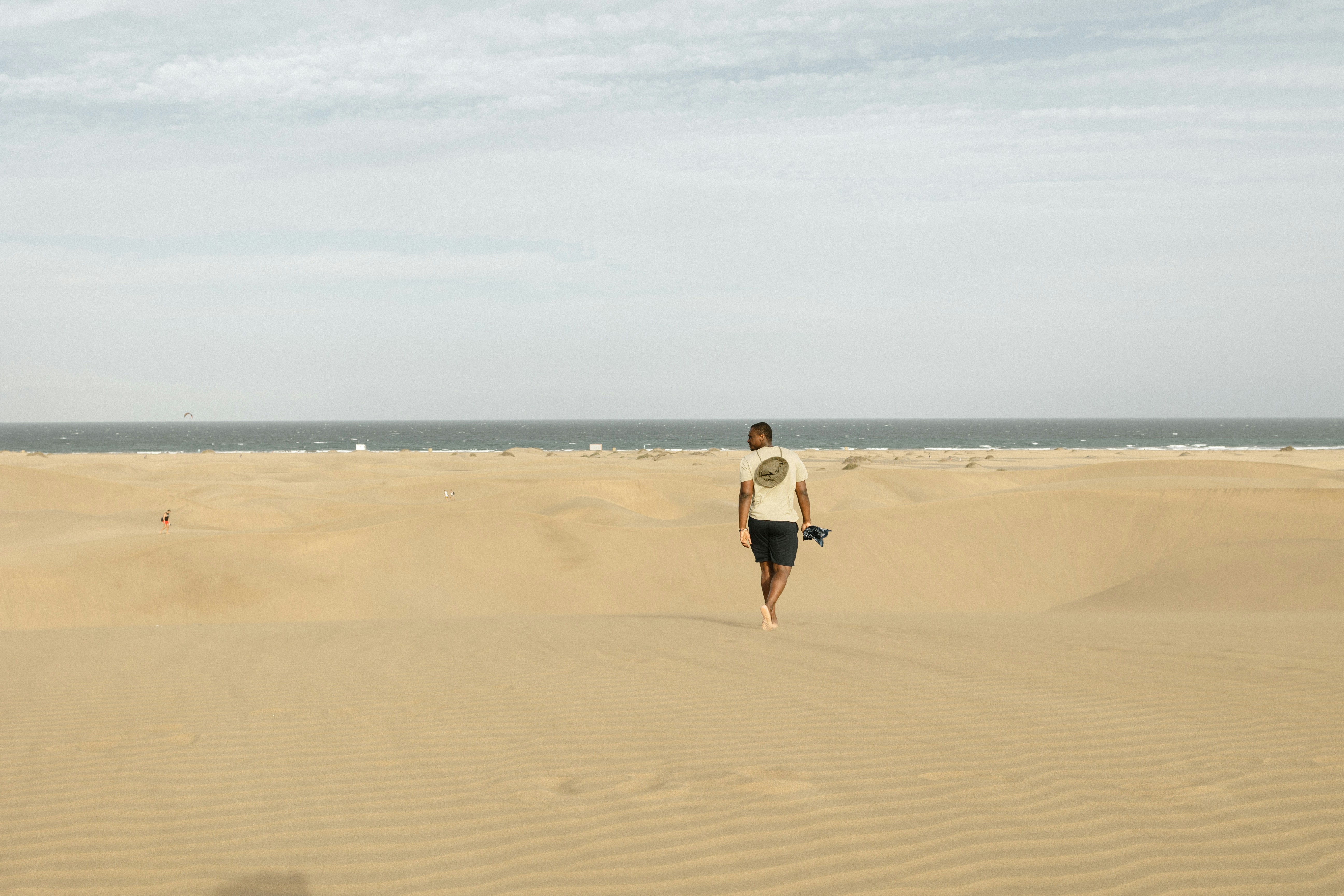 Femme en chemise blanche et short noir marchant sur le sable brun pendant la journée