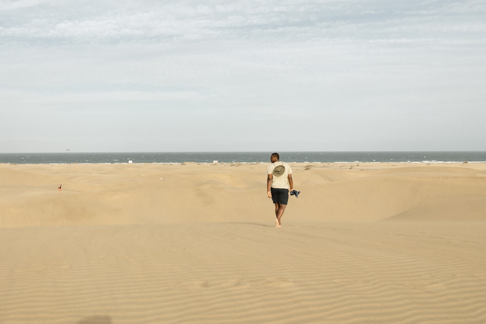 woman in white shirt and black shorts walking on brown sand during daytime