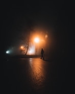 A shadowy figure walking along a foggy city street at night.