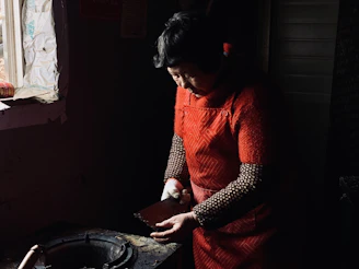 A young caregiver helping a senior woman with household chores in a bright, cozy living room.