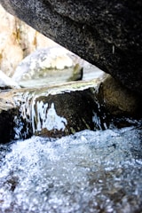 Close-up shot of icy glacial water flowing over smooth, dark stones.