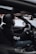 A person wearing a black helmet and gloves is driving a car with a manual transmission. They are seated in the driver's seat, holding the steering wheel, and the gear stick is visible. The interior of the car is modern and includes visible features such as the dashboard and rearview mirror.