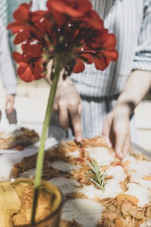 Close-up of a hand slicing a vegetable-topped pizza on a ceramic plate.