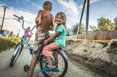 Smiling children riding bicycles along a quiet neighborhood path.