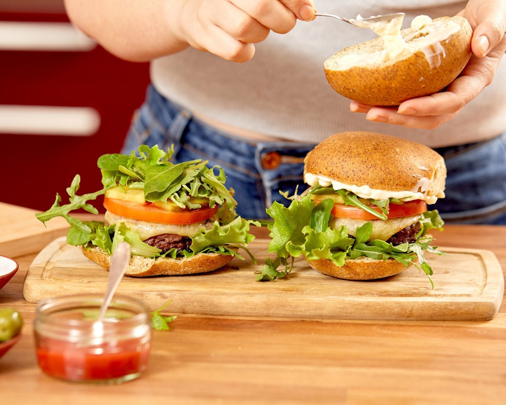 person holding burger with lettuce and tomato