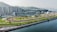 An expansive horse racing track set against a backdrop of high-rise buildings and lush green hills. The area is well-organized with clear visibility of different lanes and seating arrangements. The atmosphere is calm and the space appears well-maintained.