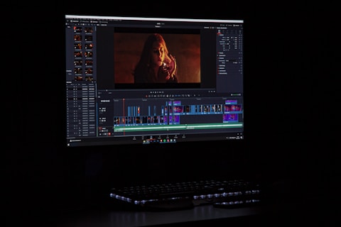 A computer monitor displays video editing software with a video track on the timeline. The screen shows various editing tools and a preview of a video featuring a person with red lighting.