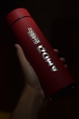 A red cylindrical tumbler featuring the AMD branding held in a hand. The lighting highlights the silver logo and text, creating a contrast against the dark background.