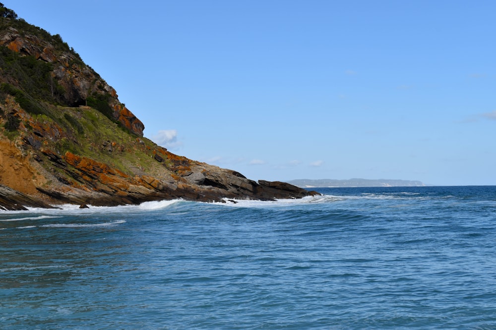 Formación rocosa marrón y verde junto al mar azul bajo el cielo azul durante el día