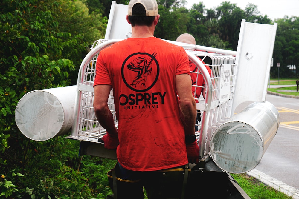 man in red crew neck t-shirt and black pants standing beside white metal fence during