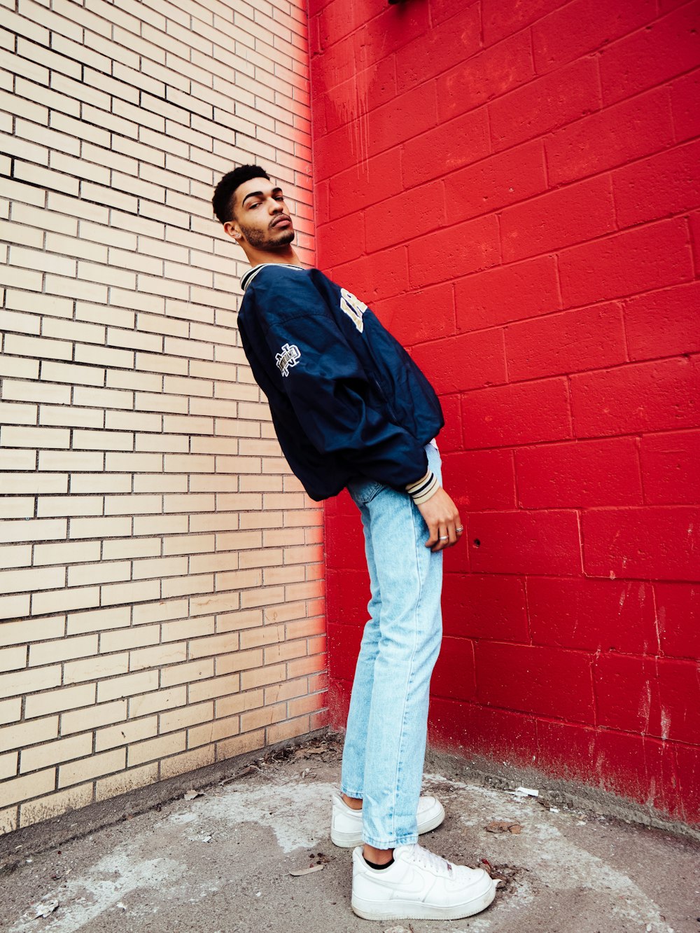 man in blue and black adidas jacket standing beside red brick wall