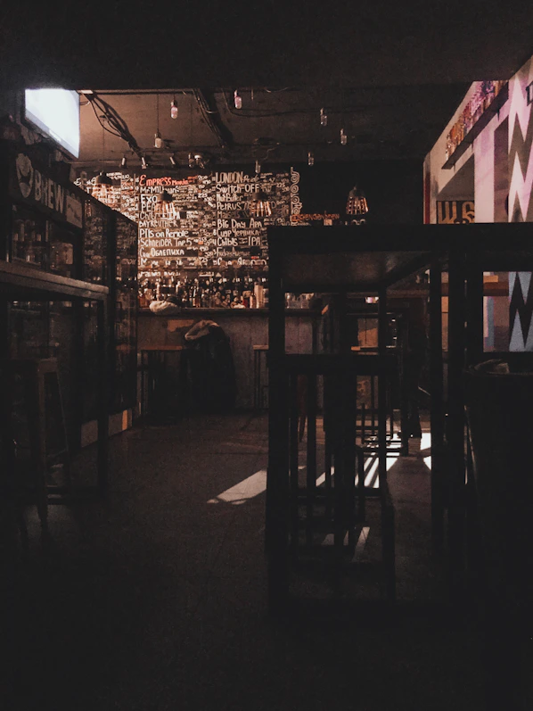 Dimly lit amber-hued cocktail bar interior showcasing exposed brick walls and moody industrial lighting.