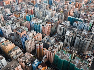 An extensive view of a densely populated urban area with numerous high-rise residential buildings in various colors, including blue, pink, beige, and white. The buildings are closely packed, creating a sense of urban density and complexity. Some buildings have visible rooftops with equipment and sight structures.