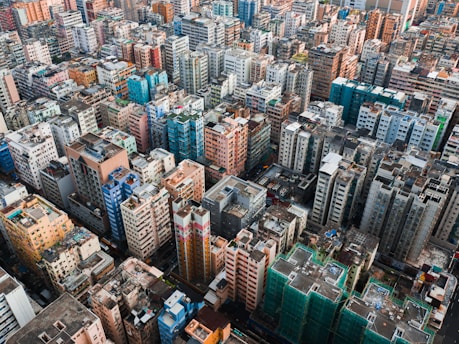 An extensive view of a densely populated urban area with numerous high-rise residential buildings in various colors, including blue, pink, beige, and white. The buildings are closely packed, creating a sense of urban density and complexity. Some buildings have visible rooftops with equipment and sight structures.
