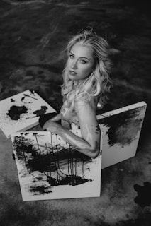 A relaxed woman sitting cross-legged on the floor, surrounded by her vibrant abstract paintings, looking peaceful and content.