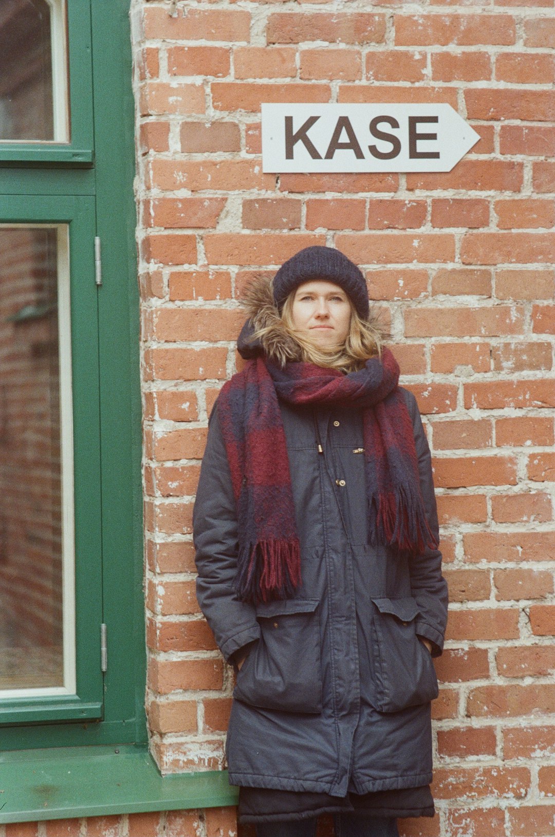 woman in red scarf and black coat standing beside brown brick wall