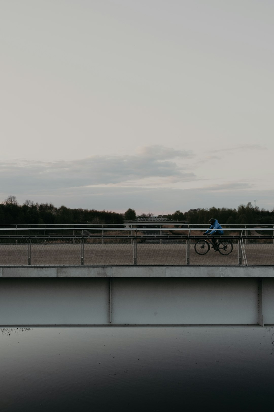 man in blue jacket riding bicycle on bridge during daytime