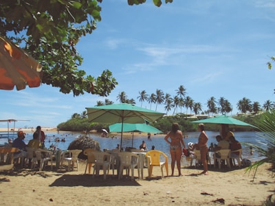 A group of friends relaxing under several Madtre umbrellas on a sunny sandy beach.