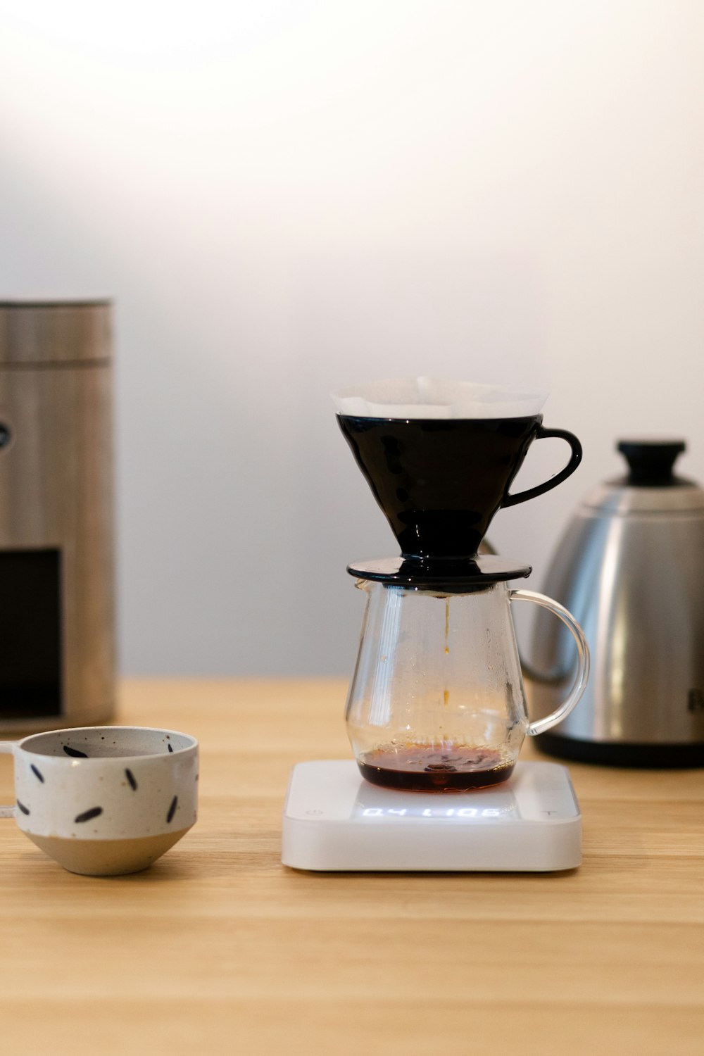 white ceramic teacup on saucer beside black coffee pot