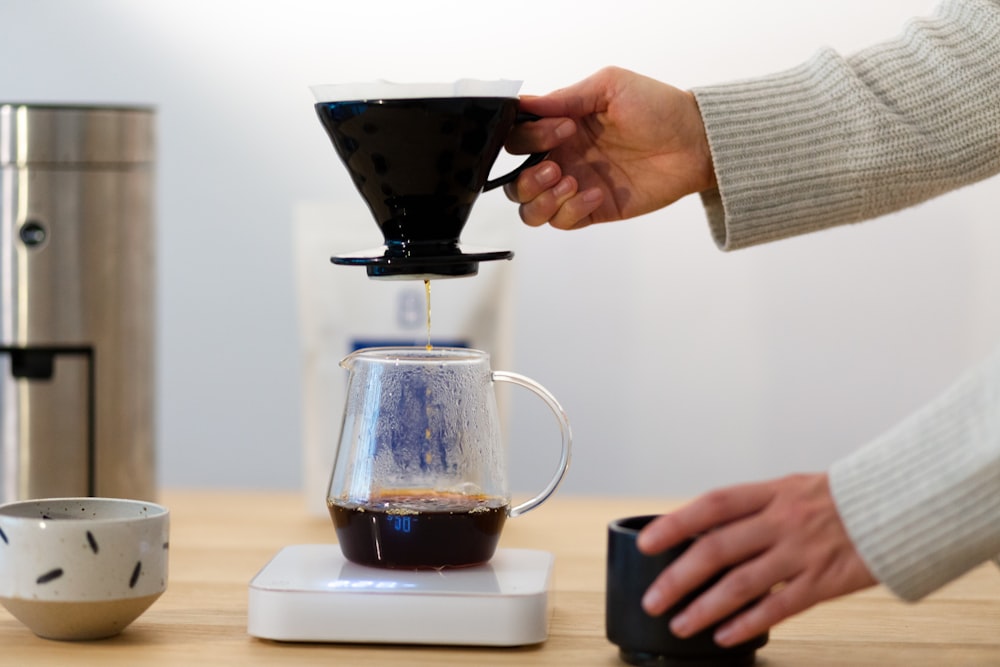 person pouring coffee on black and white ceramic cup