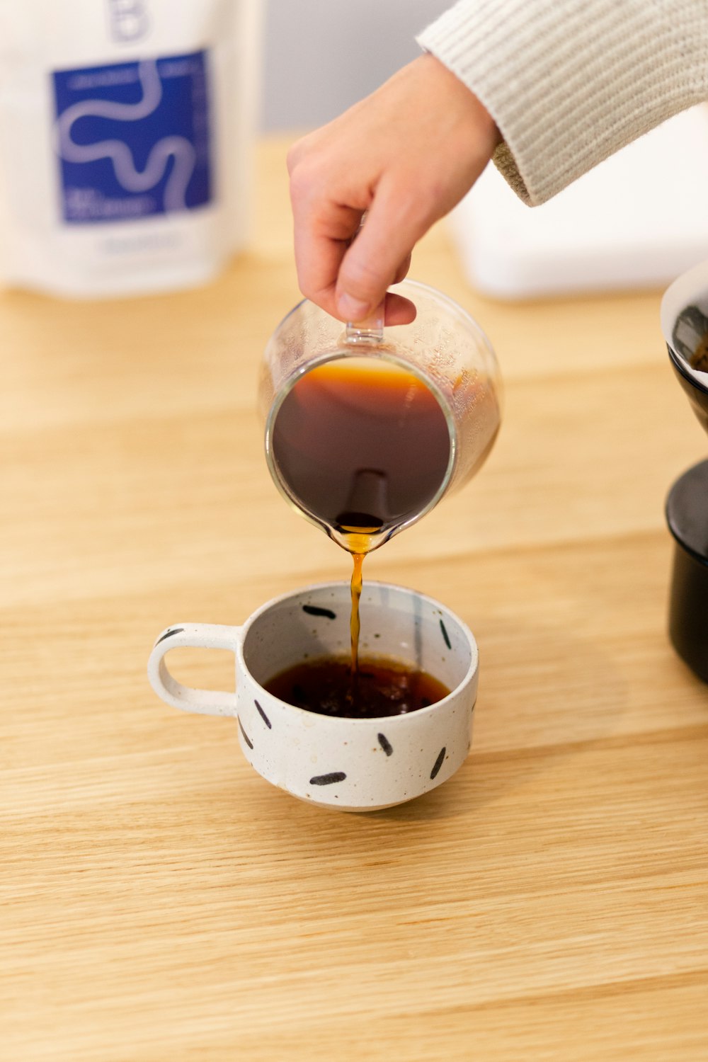 person pouring brown liquid on clear glass mug