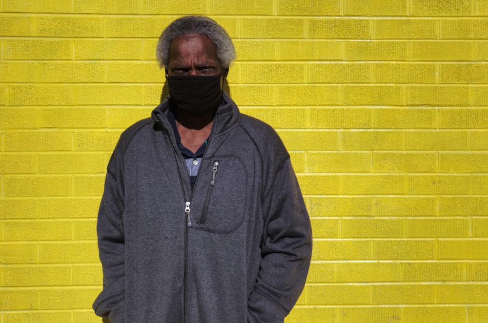 man in black zip up jacket standing beside yellow brick wall