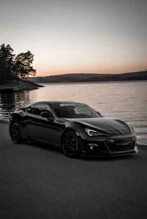 A sleek convertible car parked by a misty lake at dawn, with soft morning light reflecting on the water