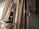 A collection of wooden planks leaning against a brick wall in a construction space. A power drill and other tools are placed on a makeshift wooden table nearby. The environment suggests an ongoing building or renovation project.