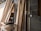 A collection of wooden planks leaning against a brick wall in a construction space. A power drill and other tools are placed on a makeshift wooden table nearby. The environment suggests an ongoing building or renovation project.