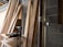 A collection of wooden planks leaning against a brick wall in a construction space. A power drill and other tools are placed on a makeshift wooden table nearby. The environment suggests an ongoing building or renovation project.