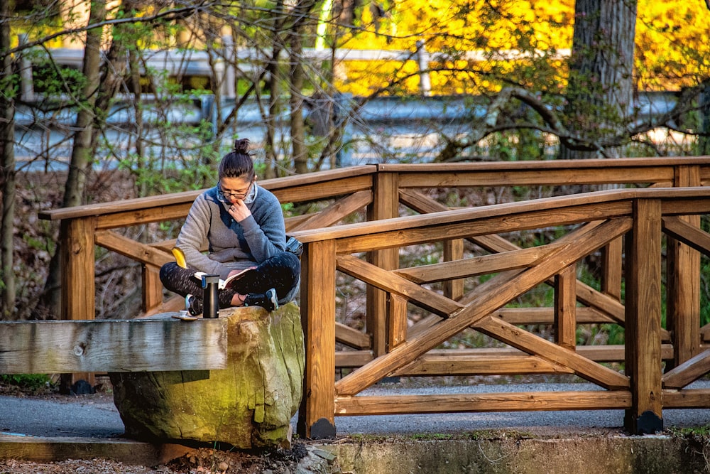 man in blue jacket sitting on brown wooden bridge during daytime