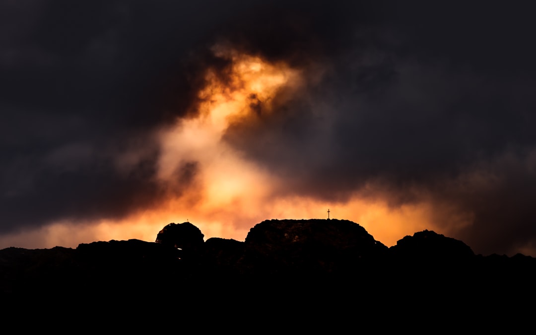 silhouette of person standing on rock formation under cloudy sky during daytime