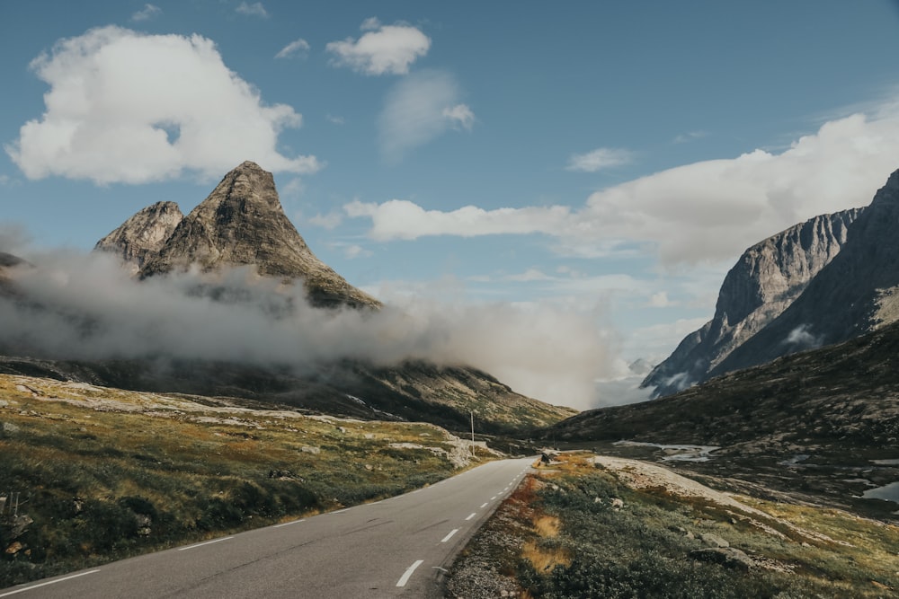 gray asphalt road near mountain under blue sky during daytime