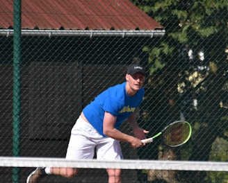 man in blue t-shirt and white pants playing tennis during daytime