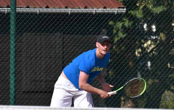 man in blue t-shirt and white pants playing tennis during daytime