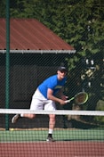 man in blue t-shirt and white pants playing tennis during daytime