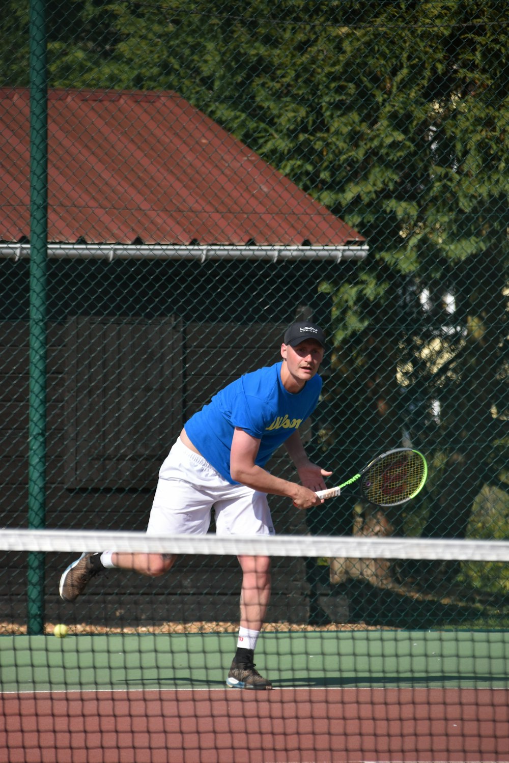 昼間にテニスをする青いTシャツと白いズボンの男