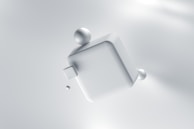 A 3D rendering of a large, smooth, metallic cube floating in a soft, light-colored space. Spherical objects are attached to the cube, creating a minimalist and futuristic appearance.