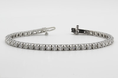 A delicate tennis bracelet featuring a series of equally sized, sparkling diamonds set in a row. The stones are mounted in a sleek metallic setting, forming an elegant and continuous line. The clasp is visible at one end, demonstrating the closure mechanism.