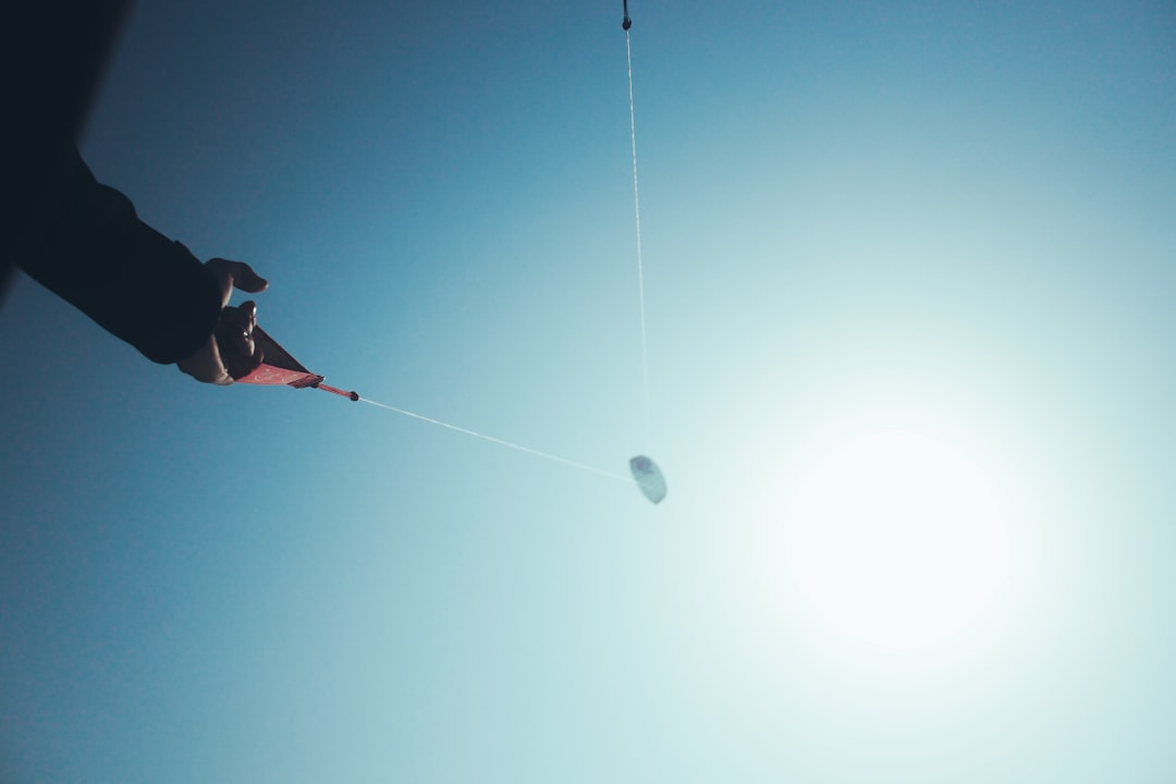 man in red shirt and black pants sitting on red and white hammock under blue sky