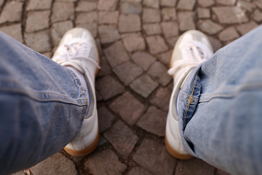 personne en jean bleu et baskets blanches