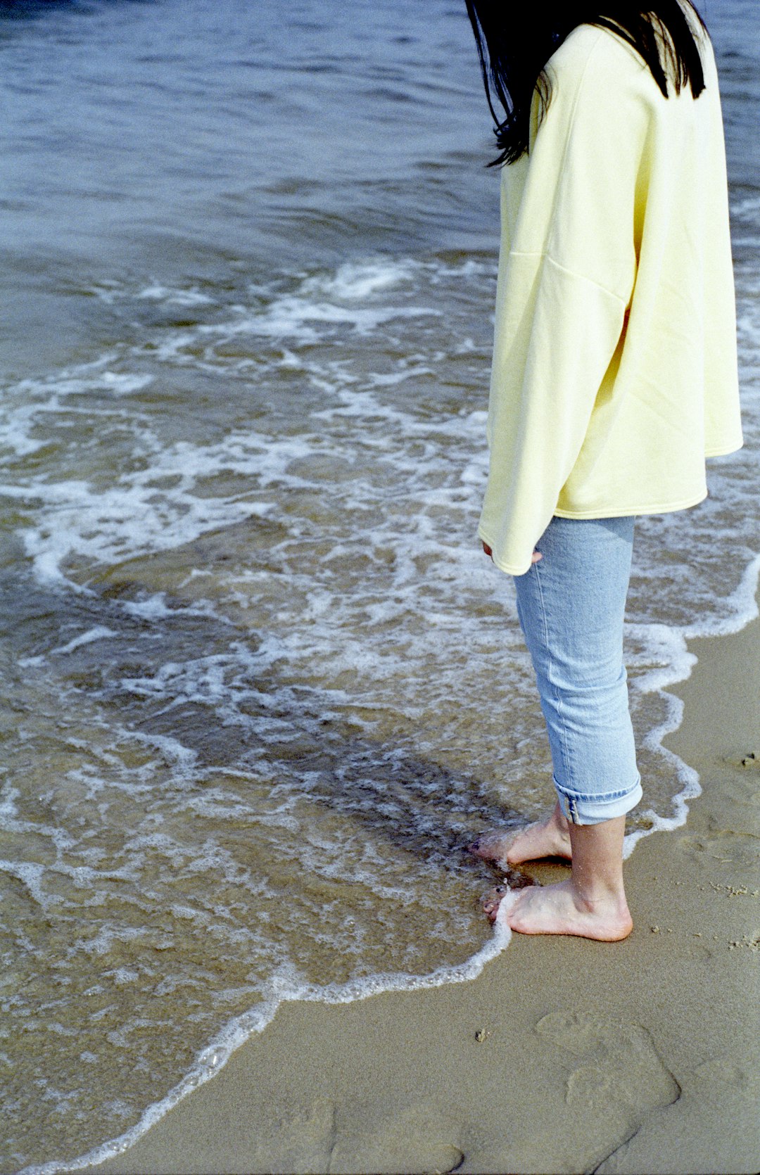 woman in yellow coat and gray pants standing on beach during daytime