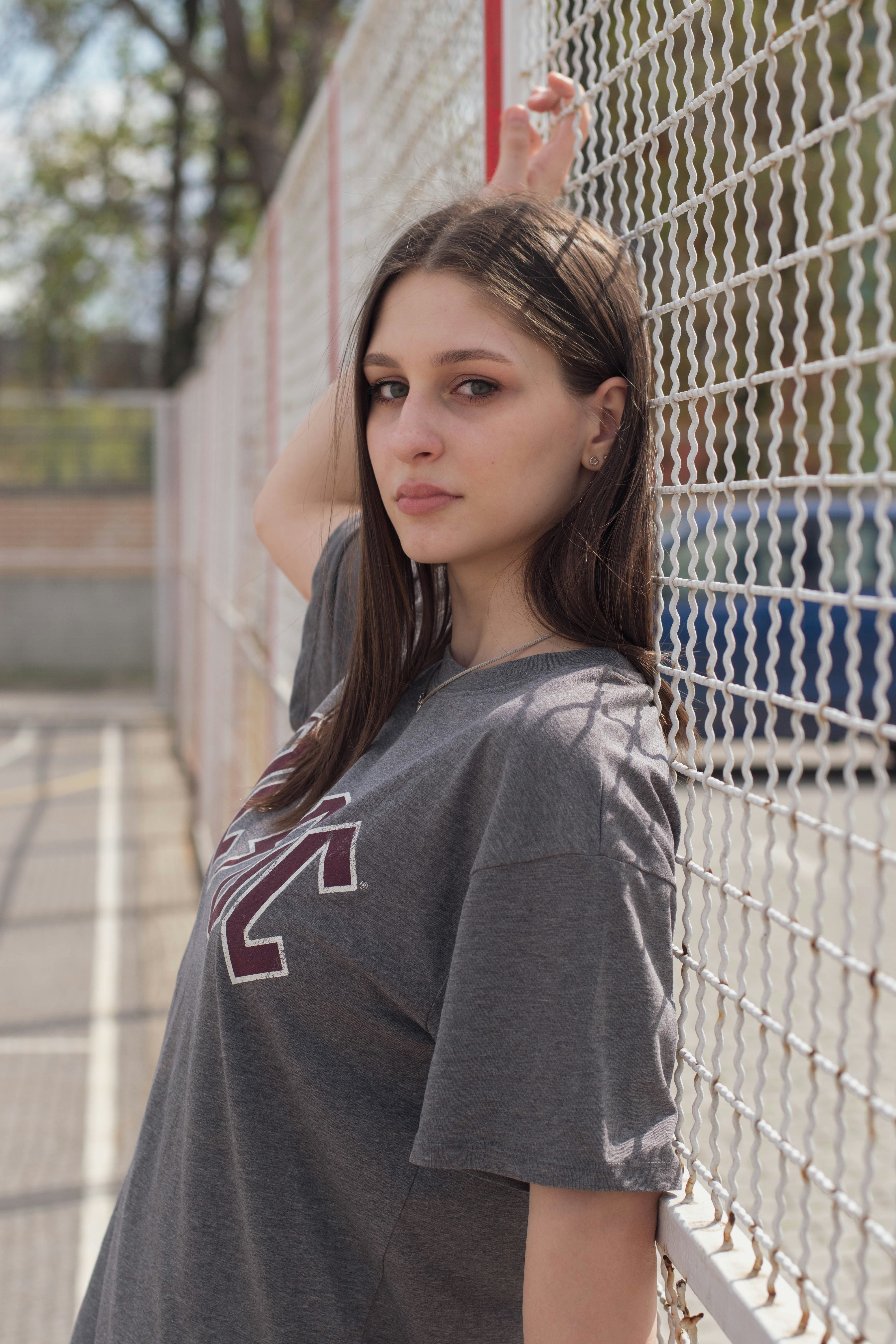 woman in gray and red hoodie standing beside chain link fence during daytime
