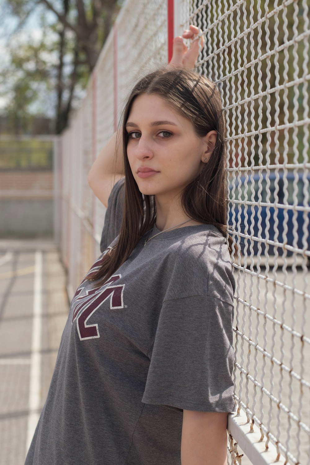 woman in gray and red hoodie standing beside chain link fence during daytime