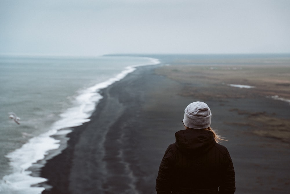 person in black jacket standing on seashore during daytime